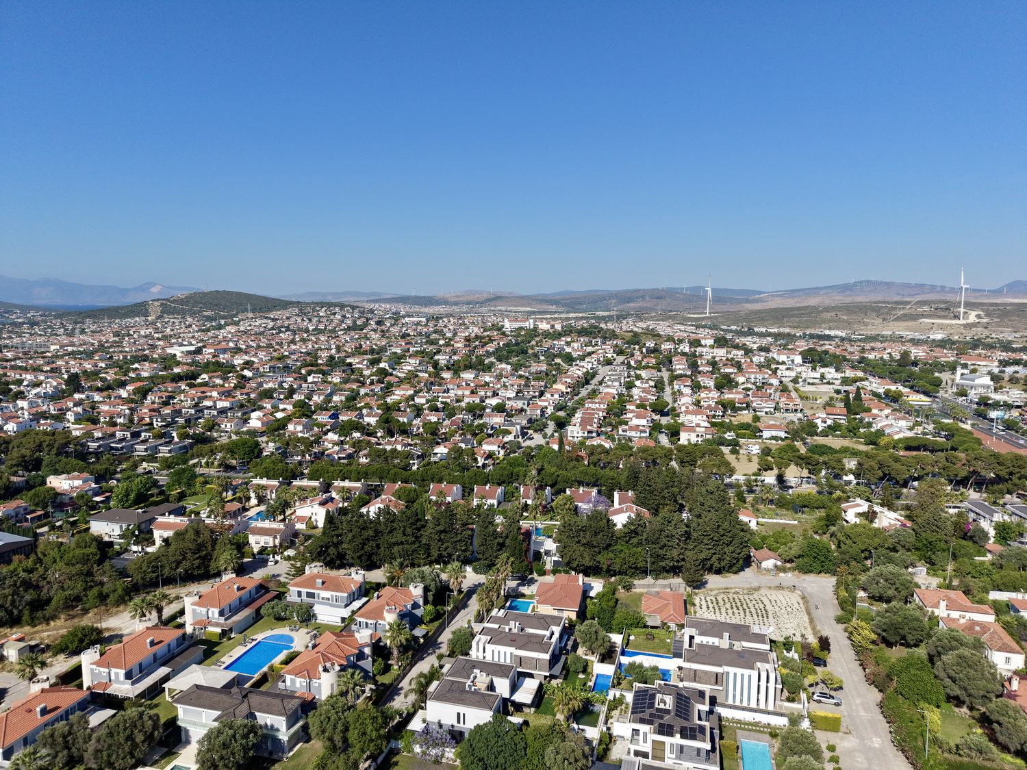 Alaçatı Göbene'nin havadan görünümü — müstakil villa dokusu, arkada Çeşme yarımadasının tepeleri
